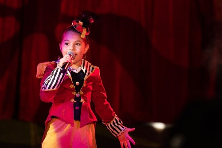 a little girl standing in front of a curtain